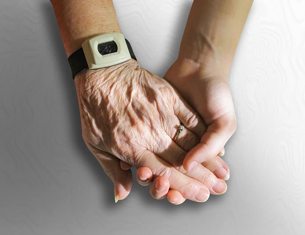 Younger person's hand holding senior citizen's hand with watch