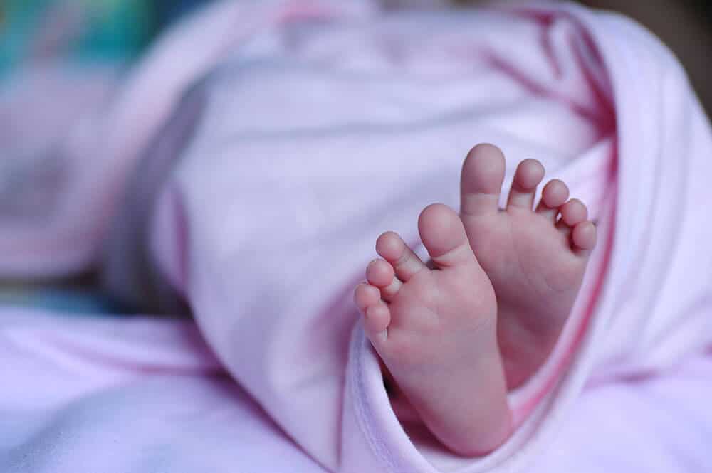 Baby wrapped in pink blanket with feet exposed