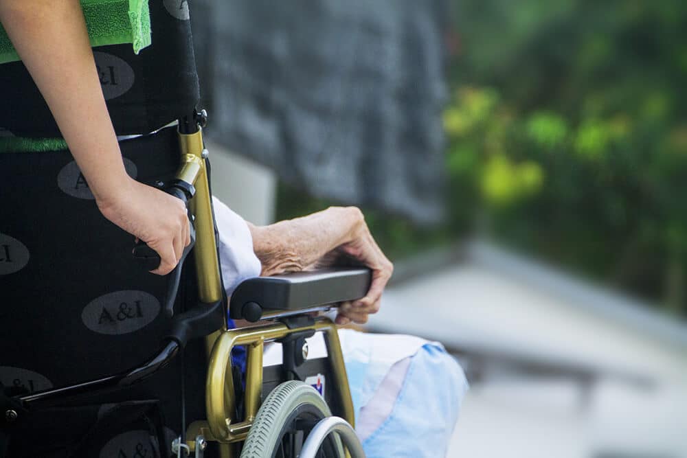 Person pushing elder in wheelchair
