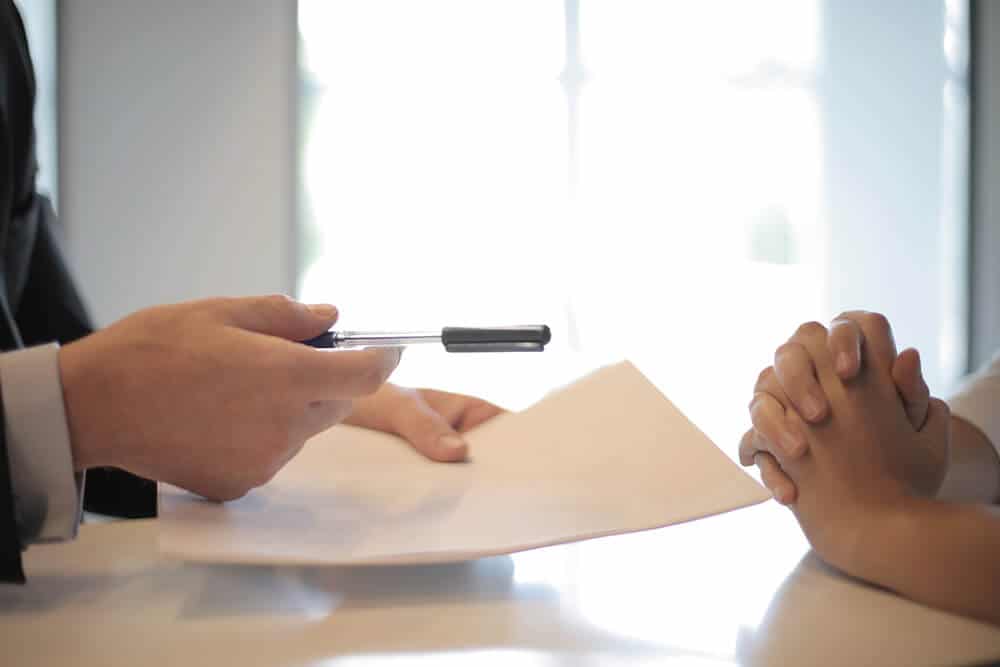 Person handing over pen and paper to other person with folded hands